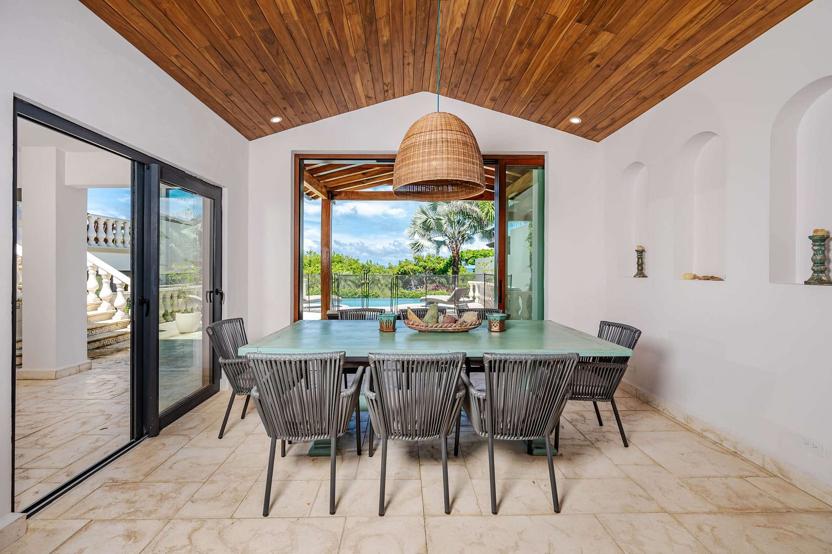 Family 8-seater dining table at Carolina del Mar surrounded by windows with a view to the outside patio and pool areas.