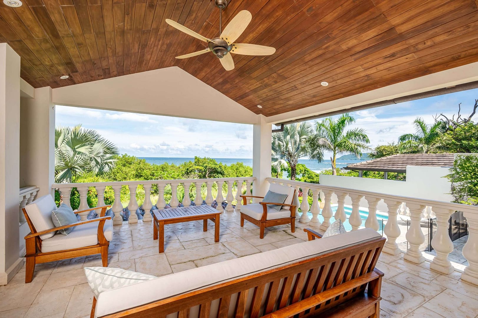 Outdoor balcony sitting area with fan and an ocean view.