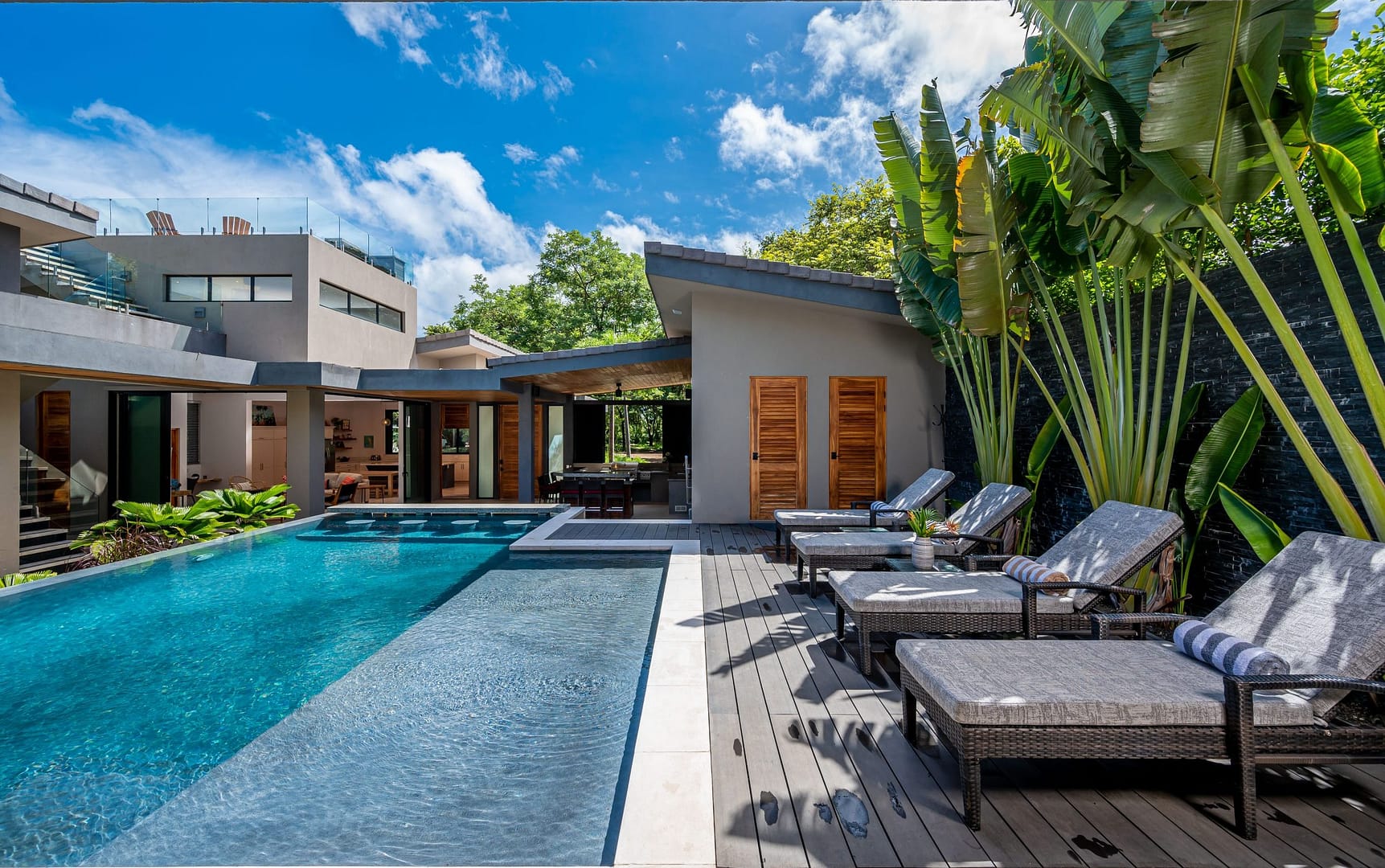 Estrella del Mar Pool with sun loungers, tropical plants, and view of the house.
