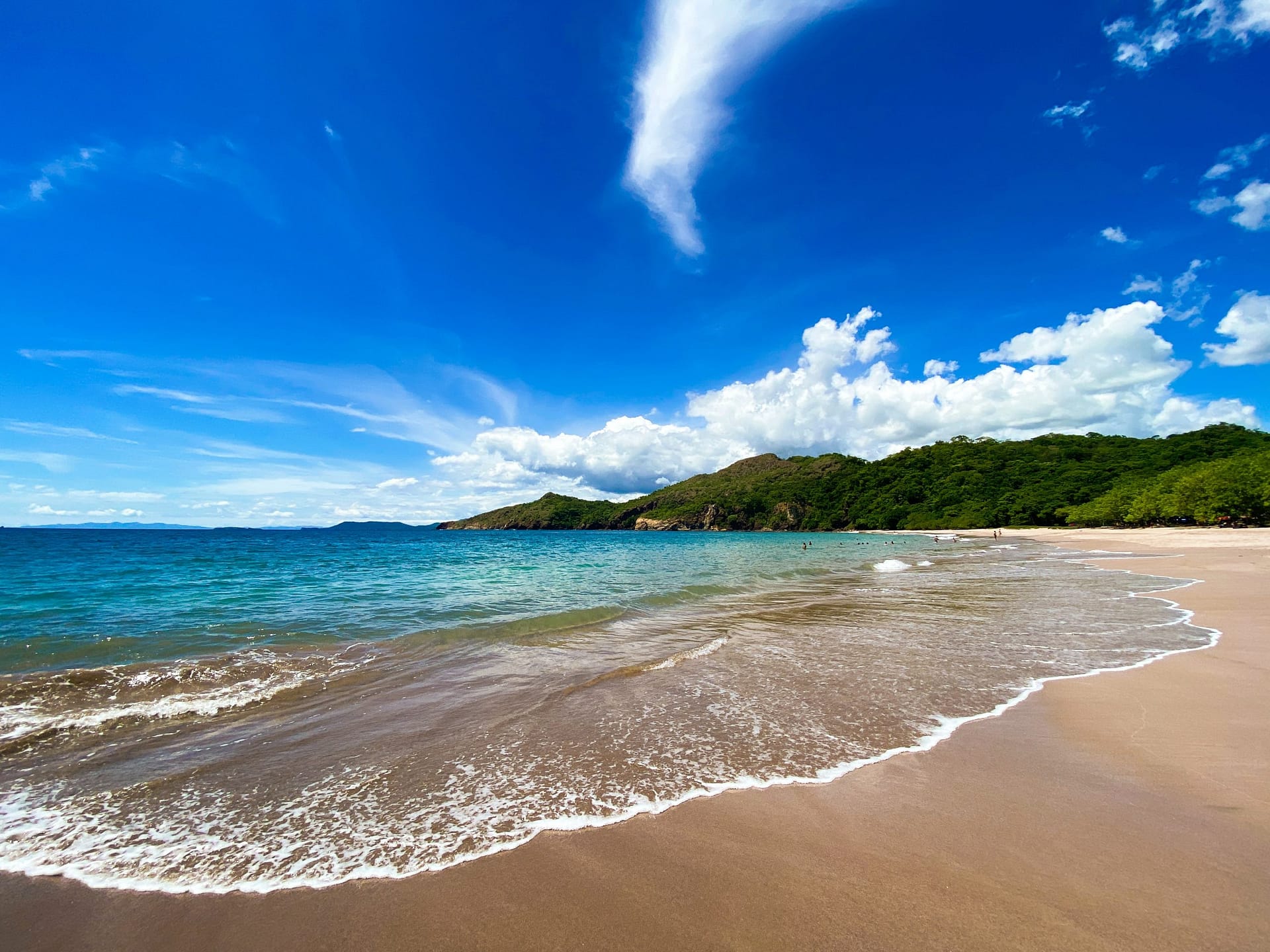 Beach with turquoise blue water and green covered hills in the distance.